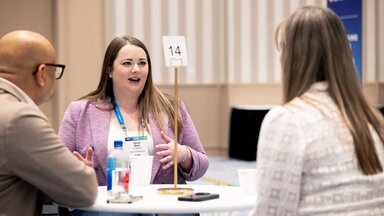 A woman is speaking expressively to two people at a networking session at HumanX 2025