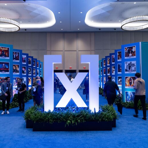 A view of the humanx logo on a pedestal with plants in the middle of the conference floor with people walking around it.