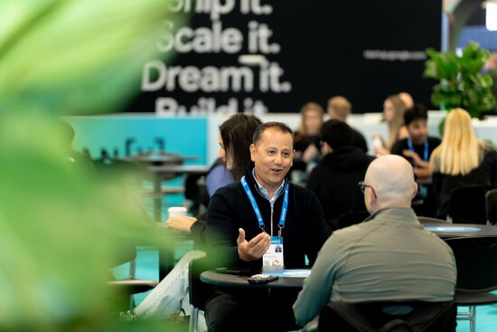 Two men network at VentureConnect at HumanX 2026 in San Francisco. People networking are seen behind them